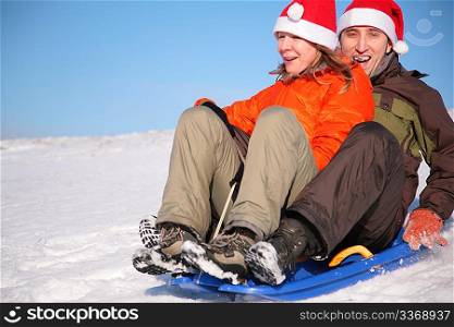 man and woman in santa claus hats ride on sled