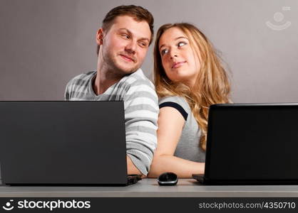 man and woman is sitting together on gray background with laptops