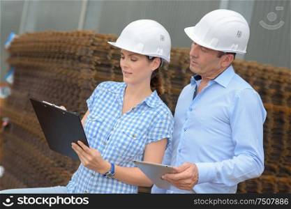 Man and woman looking at clipboard next to building materials