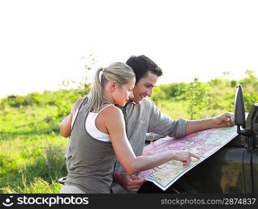 Man and woman looking at map on bonnet of jeep