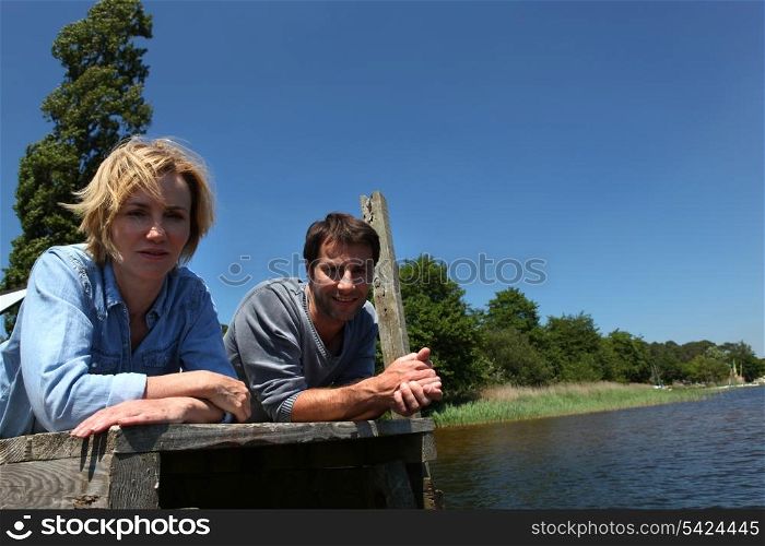 Man and woman lying on a wooden jetty on a blue sky day