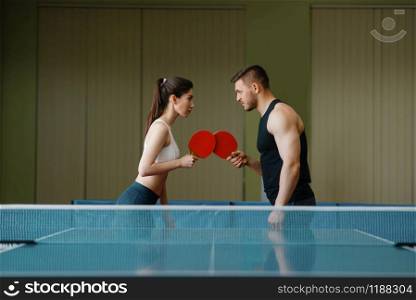 Man and woman on ping pong training indoors. Couple in sportswear holds rackets and plays table tennis in gym. Male and female persons in table-tennis club. Man and woman on ping pong training indoors