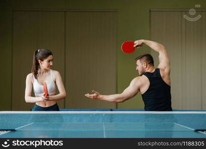 Man and woman on ping pong training indoors. Couple in sportswear holds rackets and plays table tennis in gym. Male and female persons in table-tennis club