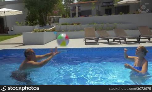 Man and woman playing ball in swimming pool in summer