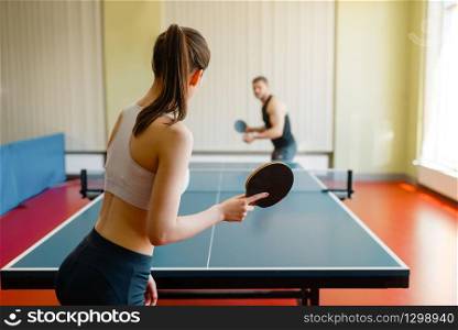Man and woman playing ping pong indoors. Couple in sportswear holds rackets and plays table tennis in gym. Man and woman playing ping pong indoors