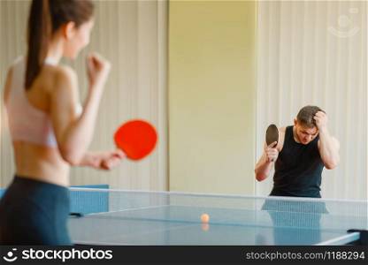 Man and woman playing ping pong indoors, girl winner. Couple in sportswear holds rackets and plays table tennis in gym