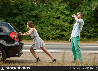 Man and woman pushing broken car on road, breakdown. Crashed automobile or emergency accident with vehicle, trouble with engine on highway. Man and woman pushing broken car on road