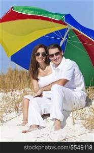 Man and woman romantic couple wearing sunglasses under a multi colored sun umbrella or parasol on a beach