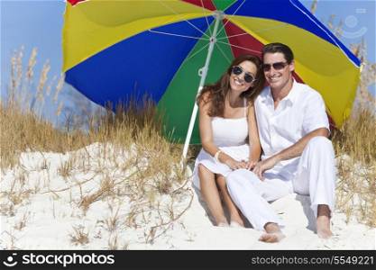 Man and woman romantic couple wearing sunglasses under a multi colored sun umbrella or parasol on a beach