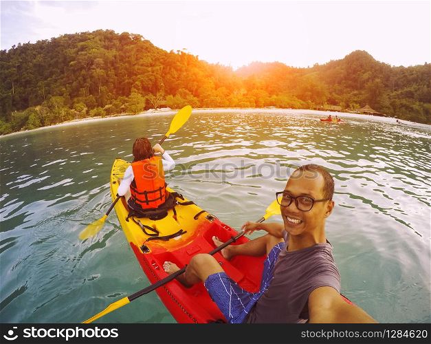 man and woman sailing sea kayak over clear water of island