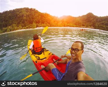 man and woman sailing sea kayak over clear water of island