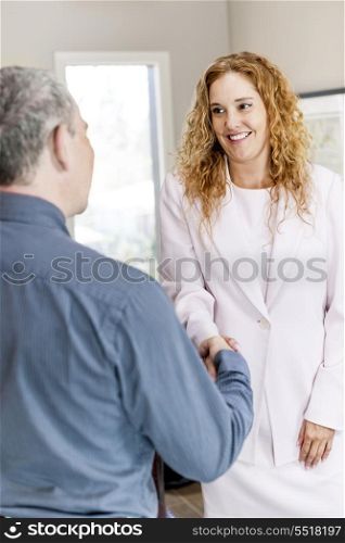 Man and woman shaking hands in office. Man and woman meeting in office shaking hands completing business deal