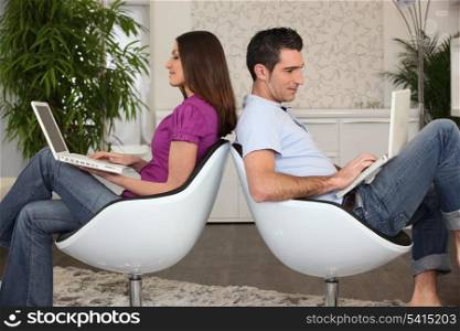 Man and woman sitting back to back using computers