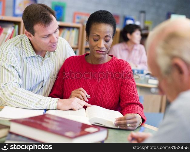 Man and woman sitting in library near man with a book and notepad (selective focus)