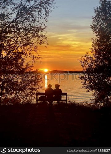 Man and woman sitting on a bench by the lake in beautiful golden summer sunset