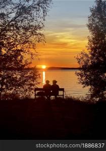 Man and woman sitting on a bench by the lake in beautiful golden summer sunset