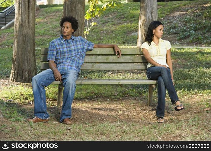 Man and woman sitting on opposite sides of park bench looking away from eachother.