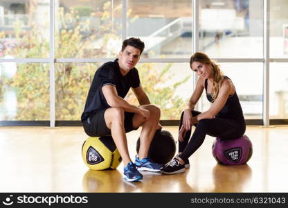 Man and Woman sitting with fitballs in the gym. Young people wearing sportswear clothes.