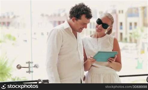 Man and woman standing on the balcony and discussing a business project using a touchpad