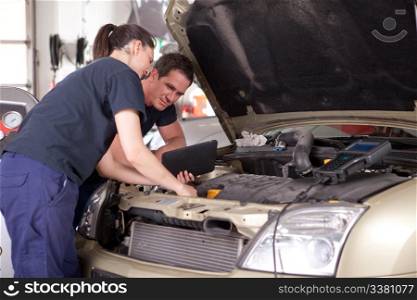 Man and woman team of mechanics using digital tablet while diagnosing car engine.