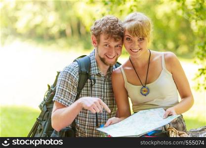 Man and woman tourists backpackers reading map on trip while resting. Young couple hikers searching looking for direction guide. Backpacking summer vacation travel.