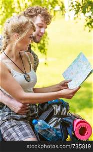 Man and woman tourists backpackers reading map on trip while resting. Young couple hikers searching looking for direction guide. Backpacking summer vacation travel.
