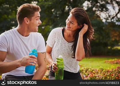 Man and woman training in park, chatting during a water break