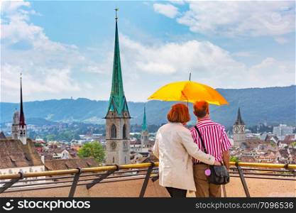 Man and woman under bright orange umbrella admire the panorama of the Old Town of Zurich, the largest city in Switzerland. Zurich, the largest city in Switzerland