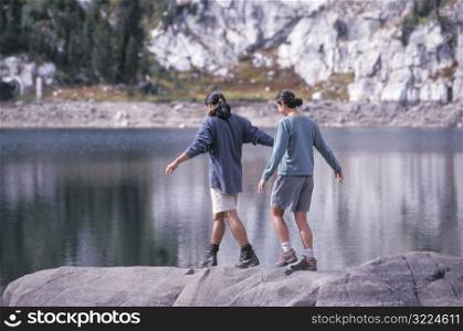 Man And Woman Walking Along A Rock In A Mountain Lake