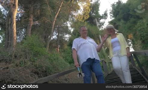 Man and woman walking in forest and taking selfie, using selfie stick. Evening.