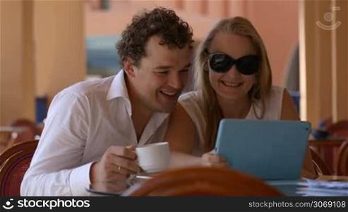 Man and woman watching photos on tablet pc having tea and kissing