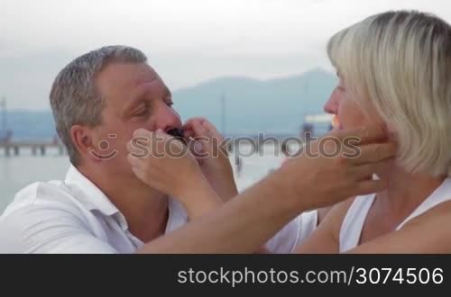 Man and woman wearing handmade moustache and having fun against of sea and mountains.