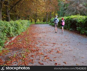 Man and woman with backpacks are walking the park alleys under chestnuts in the late summer