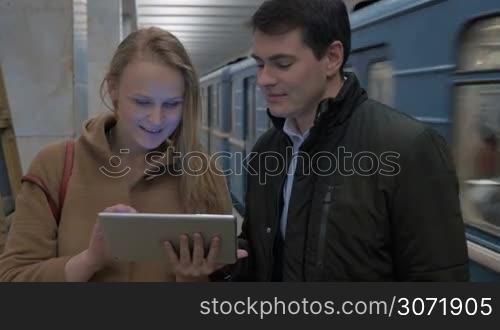 Man and woman with touch pad in the underground. Woman showing something on pad and they discussing it. Leaving train in background