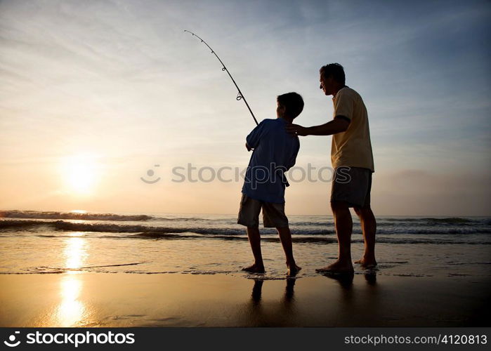 Man and young boy fishing in surf