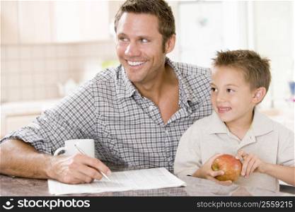 Man and young boy in kitchen with newspaper apple and coffee smiling