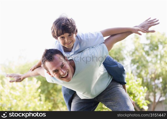 Man and young boy outdoors playing airplane smiling