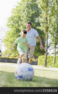 Man and young boy outdoors playing soccer and having fun