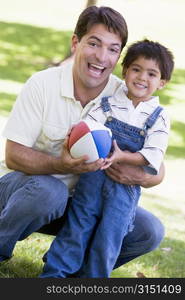 Man and young boy outdoors with football smiling