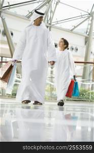 Man and young boy walking in mall holding hands and smiling (selective focus)