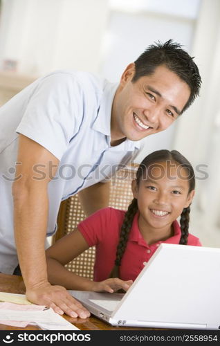 Man and young girl with laptop in dining room smiling