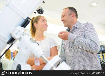 Man and young lady stood next to a telescope