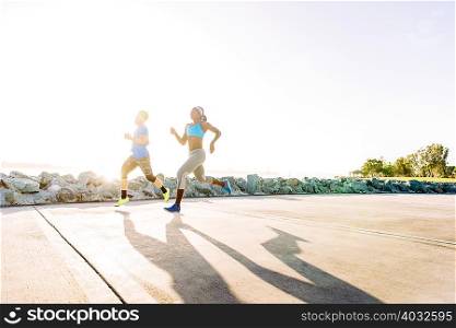 Man and young woman training, running on sunlit coast, downtown San Diego, California, USA