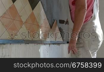 man applying ceramic tile to a Kitchen wall, working with trowel, Medium Shot