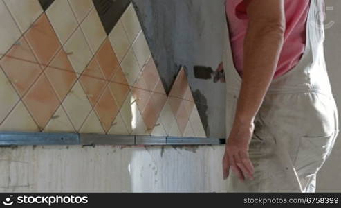 man applying ceramic tile to a Kitchen wall, working with trowel, Medium Shot