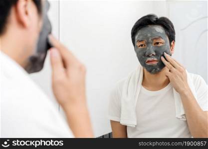 man applying facial mask in the bathroom mirror