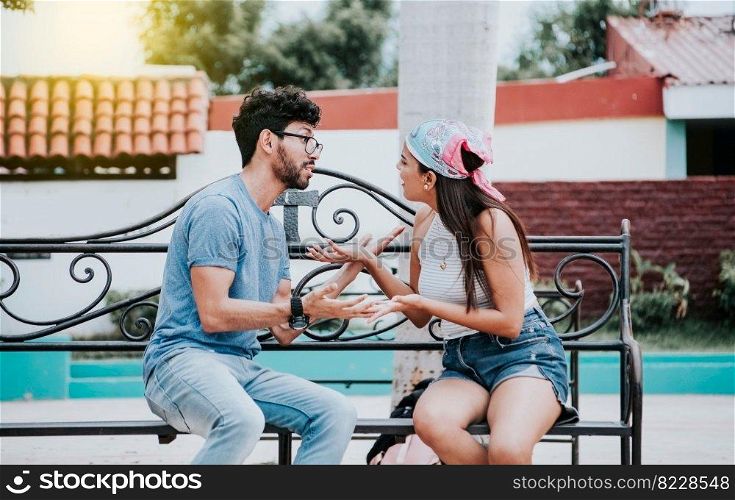 Man arguing with his girlfriend sitting in a park. Young couple arguing sitting on a park bench, Concept of aggressive couples in the park. Upset couple arguing on a park bench