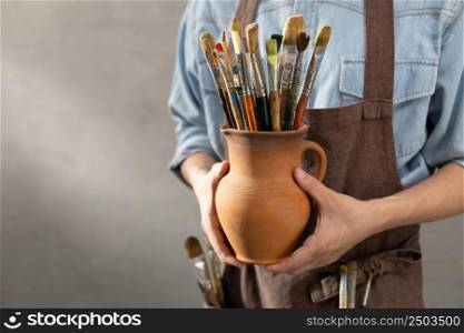 Man artist painter holding clay jug with paint brush. Painter artist and paintbrush in creative studio as art concept