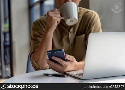 man asian drinking coffee and looking mobile phone computer laptop and at desk. Business technology digital checking emails or browsing social media while taking a quick coffee break.
