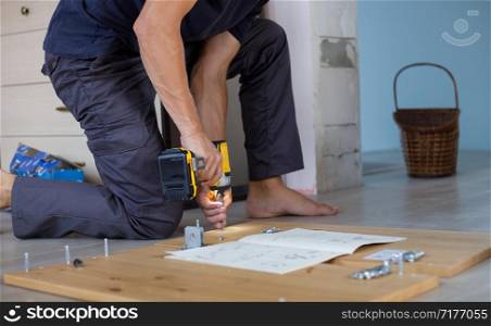 Man assembling furniture at home using a cordless screwdriver.. Man assembling furniture at home using a cordless screwdriver